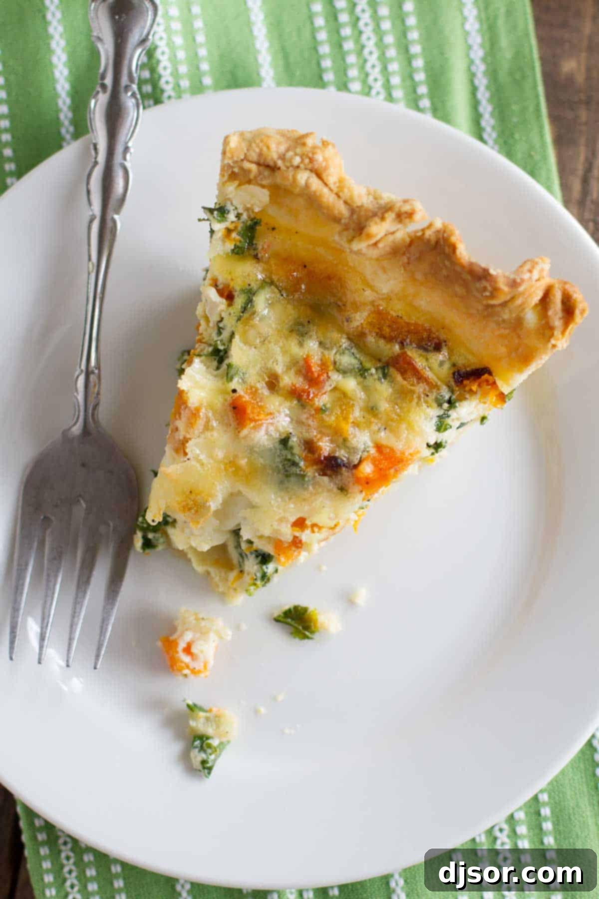 A perfect bite of Butternut Squash Quiche with Kale, showcasing its delightful filling. A close-up of a delectable slice of butternut squash quiche with kale on a plate, showing a bite taken, revealing the rich texture and colorful filling.