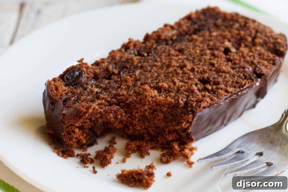 A perfectly sliced piece of Chocolate Pound Cake, revealing its dense, moist crumb, rich dark chocolate chips, and topped with a glossy dark chocolate glaze. A small bite has been taken, hinting at its deliciousness.