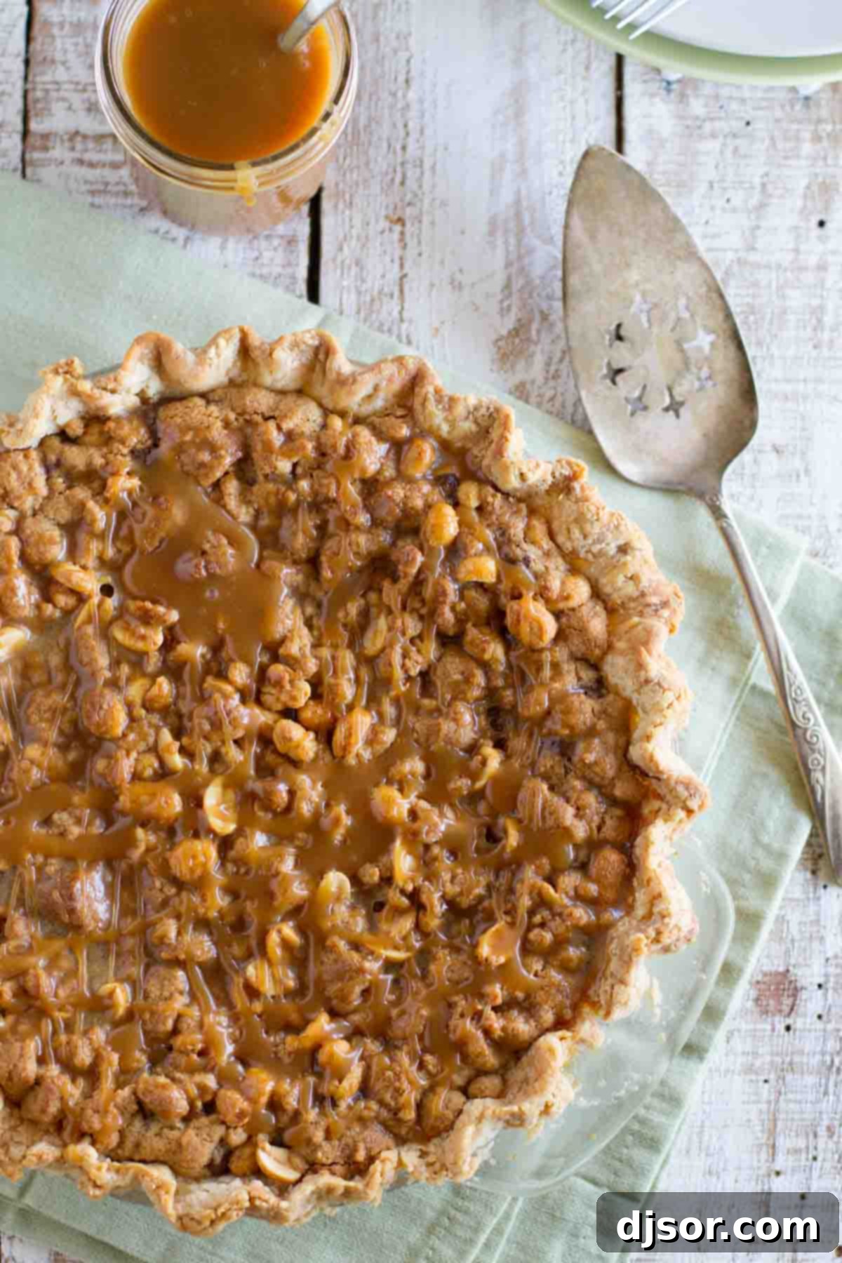 A decadent Peanut Butter Fudge Pie, generously drizzled with salted peanut butter caramel and garnished with roasted peanuts. Peanut Butter Fudge Pie with caramel and peanuts on top, presented beautifully on a serving dish.
