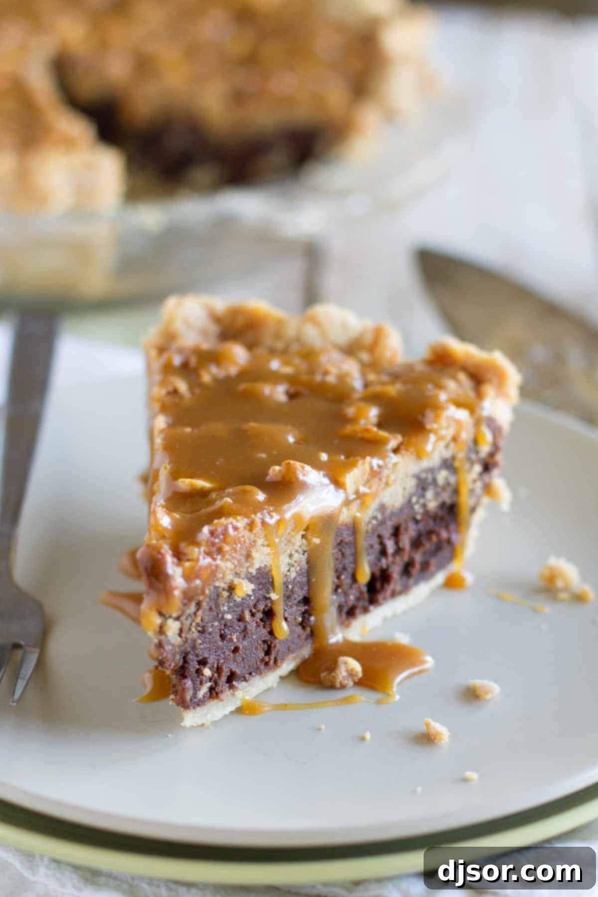 Every detail matters: a perfect slice of Peanut Butter Fudge Pie, layered with fudge, crumble, and caramel. A close-up of a slice of Peanut Butter Fudge Pie, showcasing its distinct layers and generous salted peanut butter caramel topping.