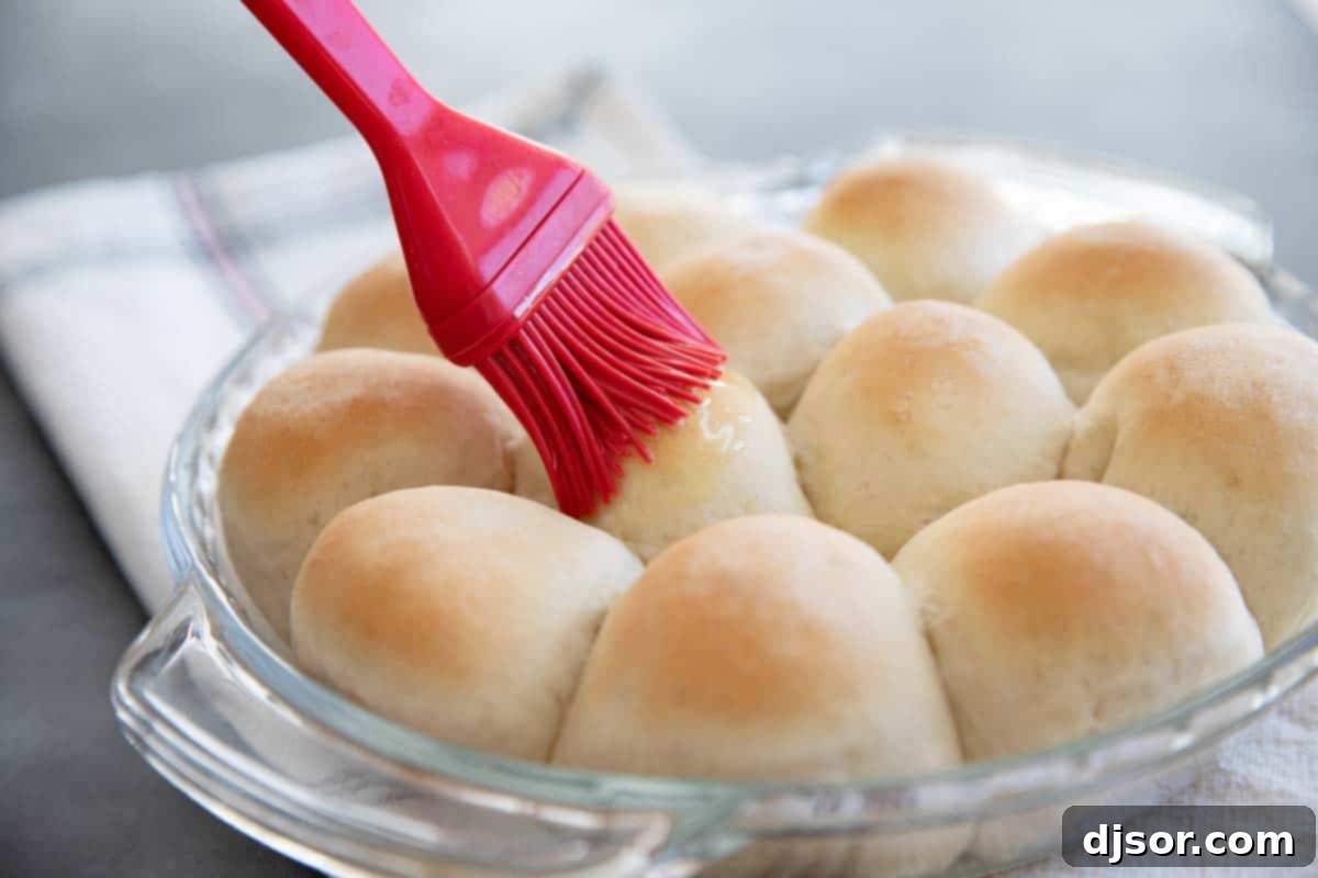Freshly baked golden dinner rolls being brushed with melted butter straight from the oven.
