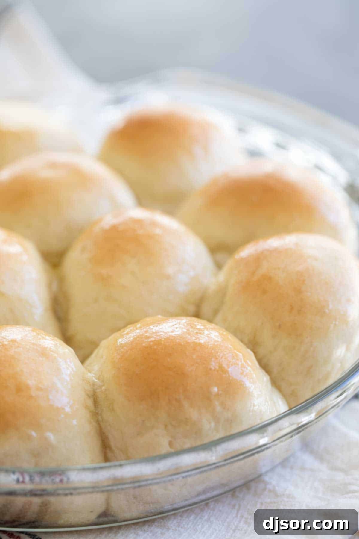 A round dish filled with golden-brown dinner rolls, glistening with melted butter.