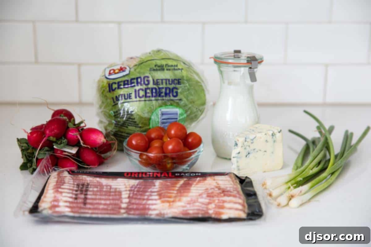 Essential ingredients for your homemade wedge salad, ready for assembly. All the fresh ingredients laid out for preparing a delicious wedge salad: a head of iceberg lettuce, a bowl of blue cheese crumbles, strips of bacon, cherry tomatoes, and green onions.
