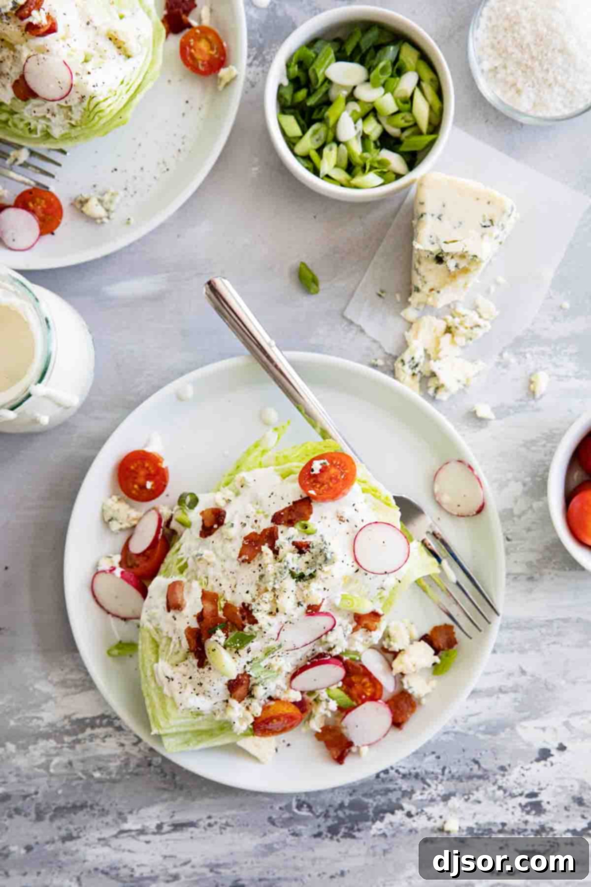 Enjoying a freshly made wedge salad, a true culinary delight with vibrant toppings. Overhead view of two wedge salads beautifully presented on white plates, garnished with blue cheese crumbles, green onions, and crispy bacon.