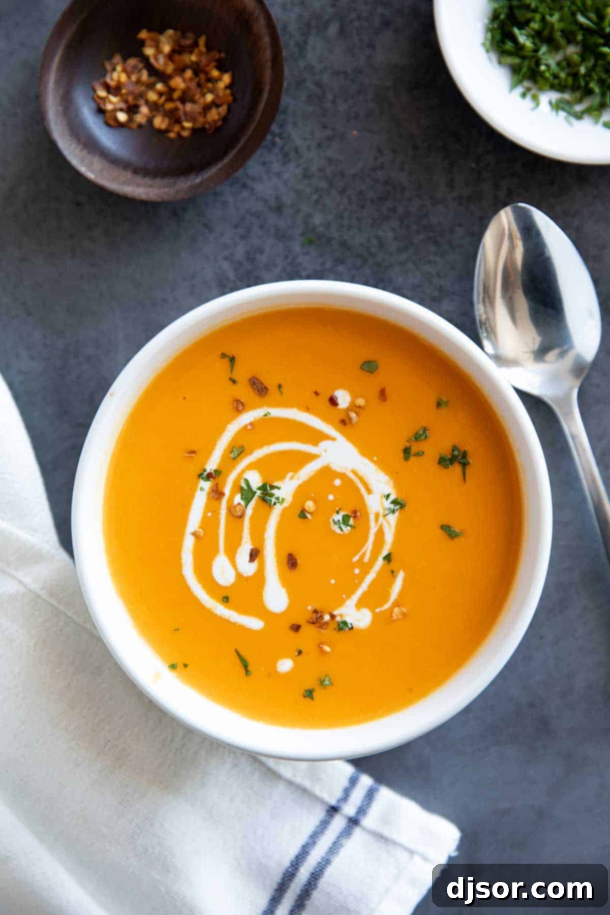 Creamy and delicious, this Sweet Potato Soup is super simple with a hint of curry and nutmeg. It is perfect as a starter, or serve it up with fresh bread for a comforting dinner. Bowl of sweet potato soup drizzled with cream.