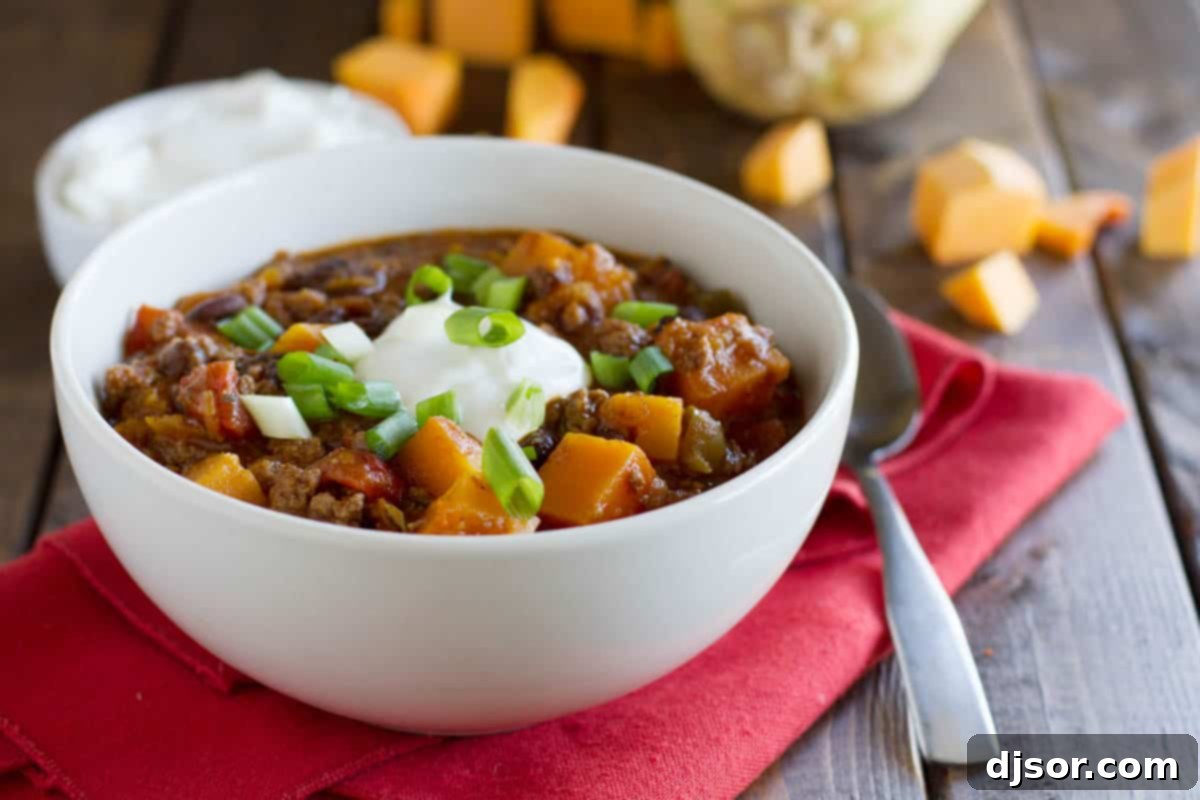 Butternut Squash Chili with Beef: A unique twist on classic comfort. A steaming bowl of butternut squash chili with beef, garnished with fresh cilantro, on a rustic red cloth.