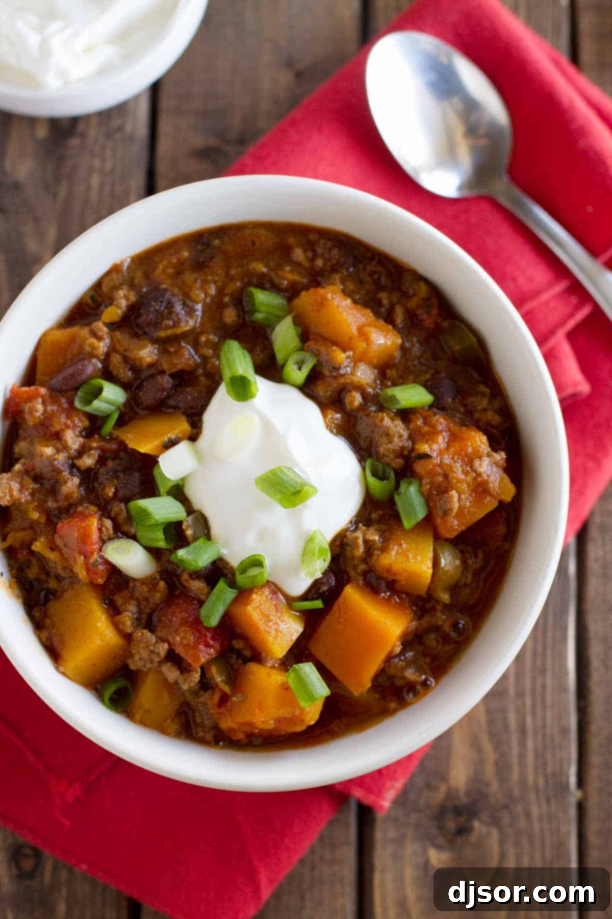 Hearty and satisfying Butternut Squash Chili with Beef. Close-up of a spoon scooping butternut squash chili with beef, beans, and vegetables from a bowl.