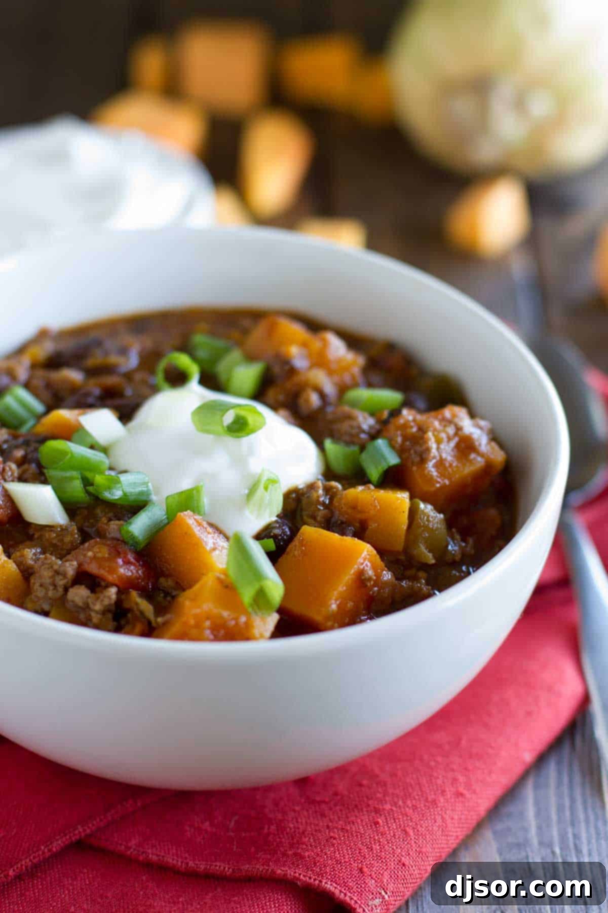 Butternut Squash Chili with Beef, garnished and ready to serve. A vibrant bowl of butternut squash chili with beef, generously topped with sour cream, fresh cilantro, and a lime wedge.