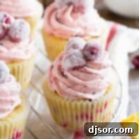 Zesty Orange Cranberry Cupcakes 2 Cranberry Orange Cupcakes on a wire rack, topped with sugared cranberries.