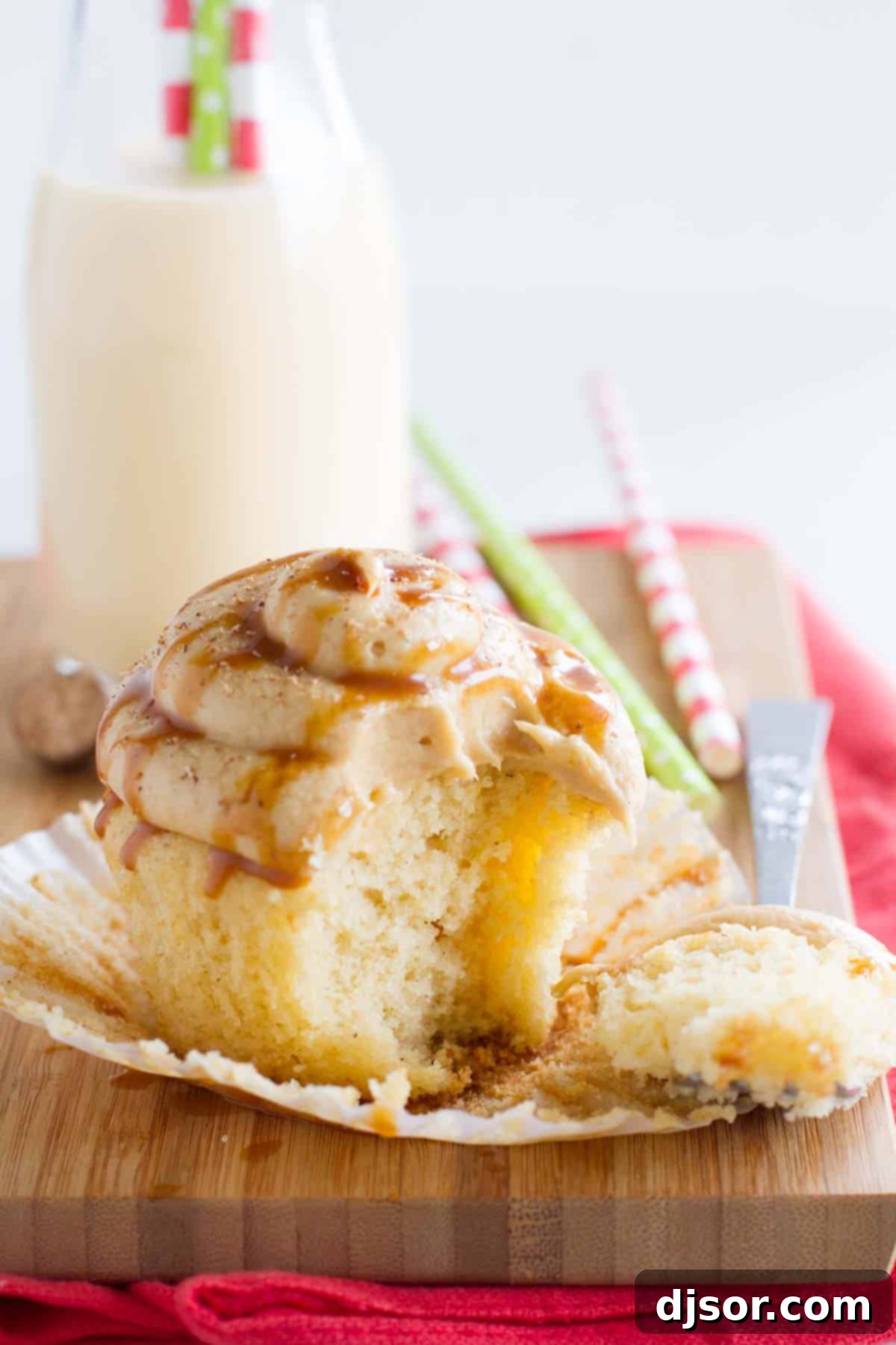 Moist and flavorful eggnog cupcakes are topped with a caramel eggnog buttercream in these festive and seasonal Eggnog Cupcakes with Caramel Eggnog Buttercream. A delicious eggnog cupcake on a cutting board, with a bite taken out, revealing its moist interior and creamy caramel eggnog buttercream.