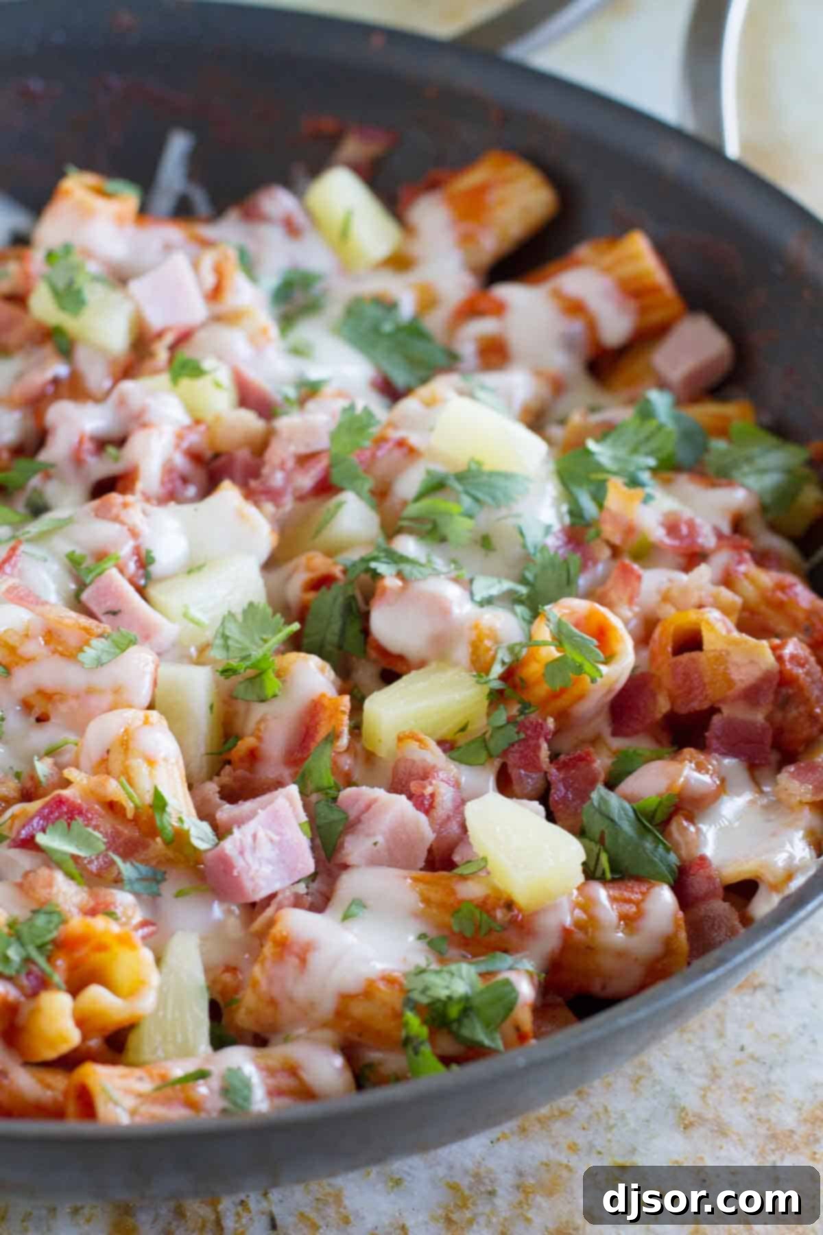 Vibrant Hawaiian One Pan Pasta, featuring succulent ham, crispy bacon, sweet pineapple chunks, and a garnish of fresh cilantro, ready to be served.