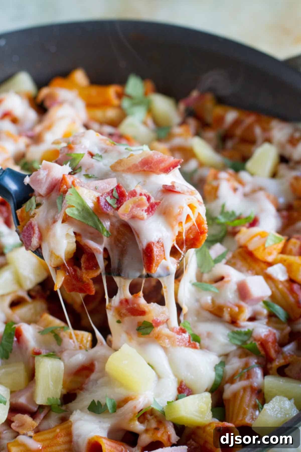 A close-up shot of a serving spoon scooping out a generous portion of warm Hawaiian One Pan Pasta, highlighting the creamy sauce and ingredients.