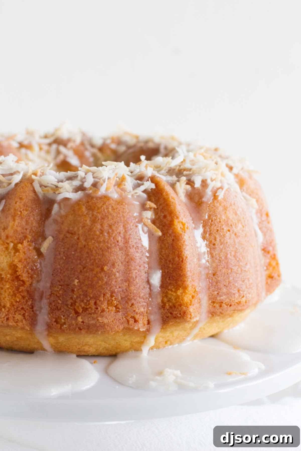 A beautifully glazed coconut bundt cake with icing drizzling down its sides, ready to be served.