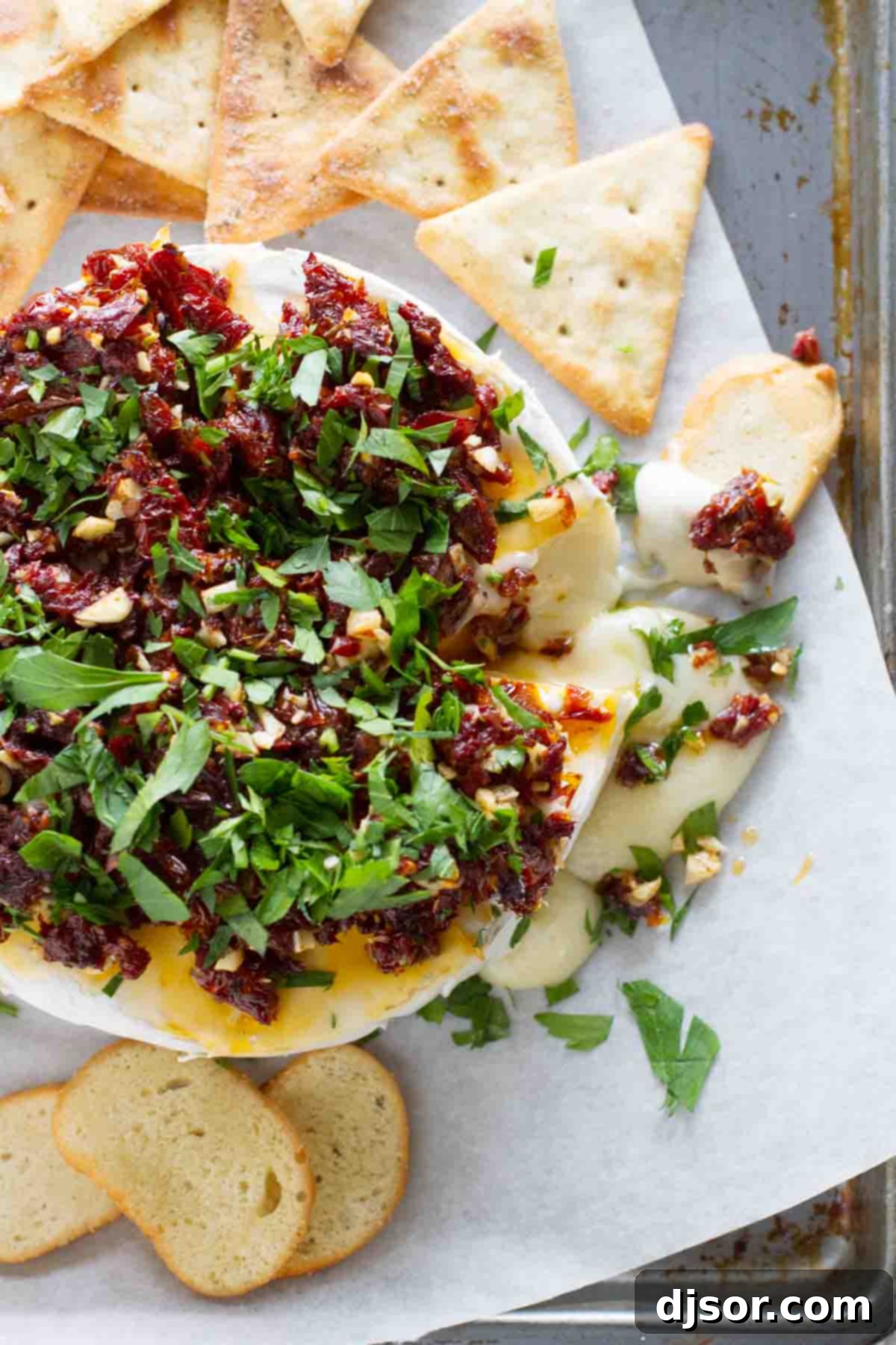 A delicious and quick appetizer for entertaining. Easy Baked Brie with Sun-Dried Tomatoes served on a platter with crackers.