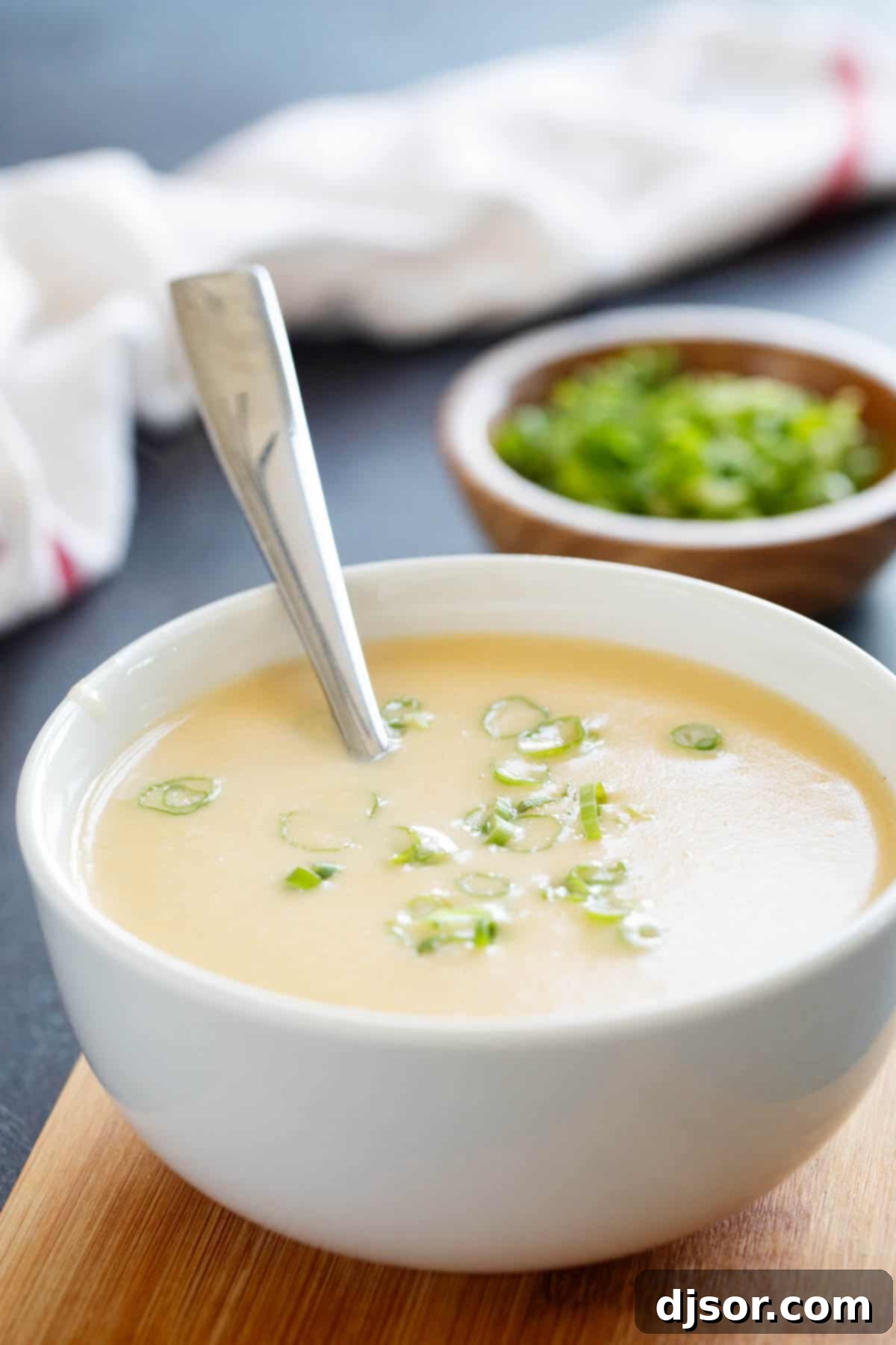 A close-up shot of a white bowl filled with creamy, golden Cheddar Cheese Soup, garnished generously with fresh green onions, ready for serving and highlighting its inviting texture.