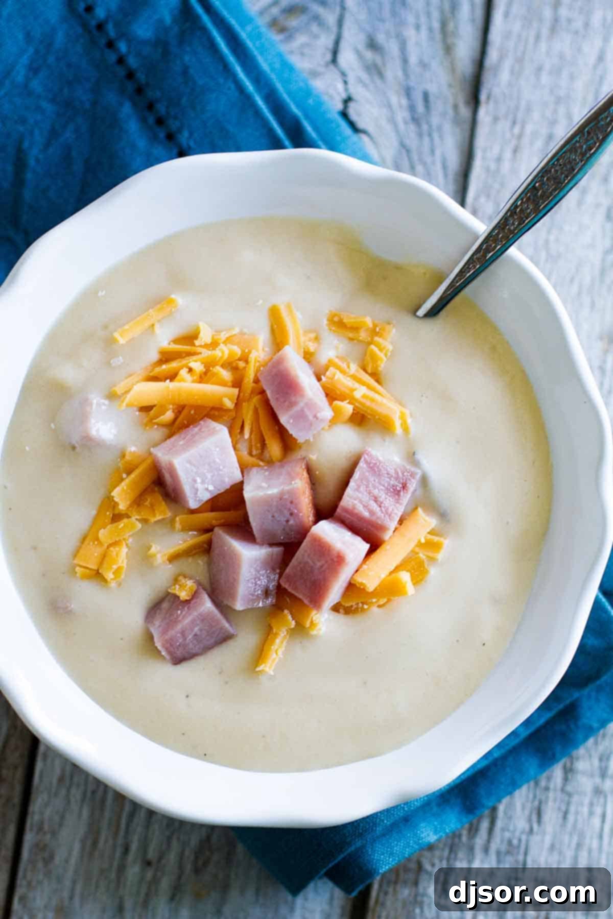 A close-up of creamy Cauliflower Soup with Ham and Cheese, ready to be enjoyed creamy cauliflower soup topped with ham and cheese in a rustic bowl