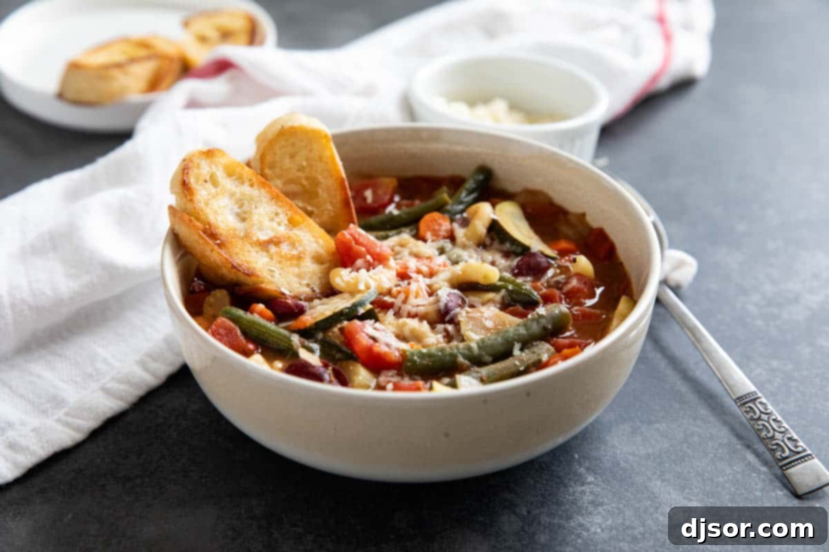 A comforting bowl of classic Minestrone Soup, generously topped with freshly grated Parmesan cheese and accompanied by golden toasted bread, ready to be enjoyed.