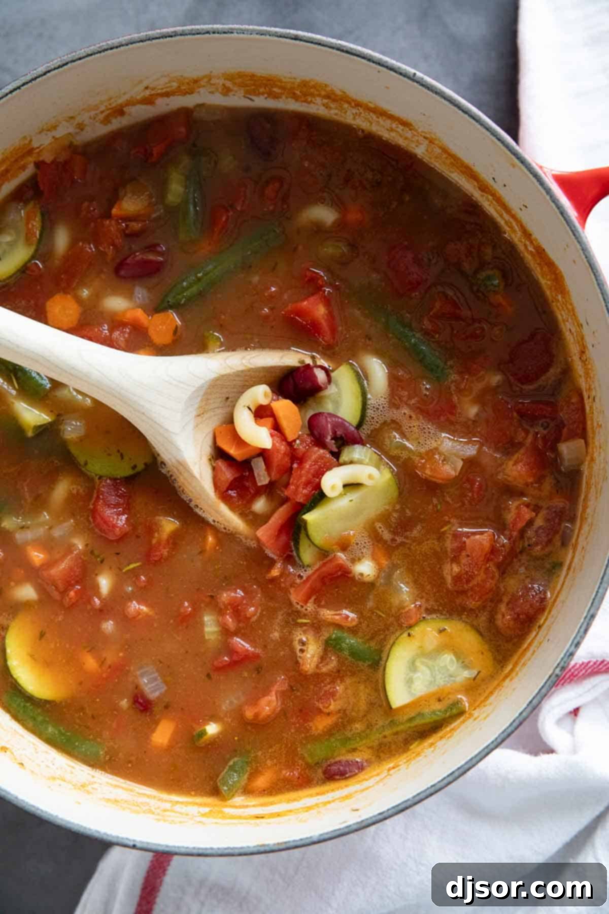 A large pot filled with steaming, rich Minestrone Soup, with a wooden spoon resting inside, highlighting the vibrant vegetables, pasta, and beans.