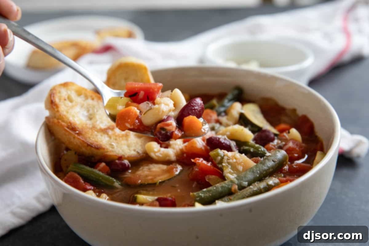 A close-up shot of a spoon filled with Minestrone Soup, showcasing the colorful mix of beans, pasta, and vegetables in the rich broth.