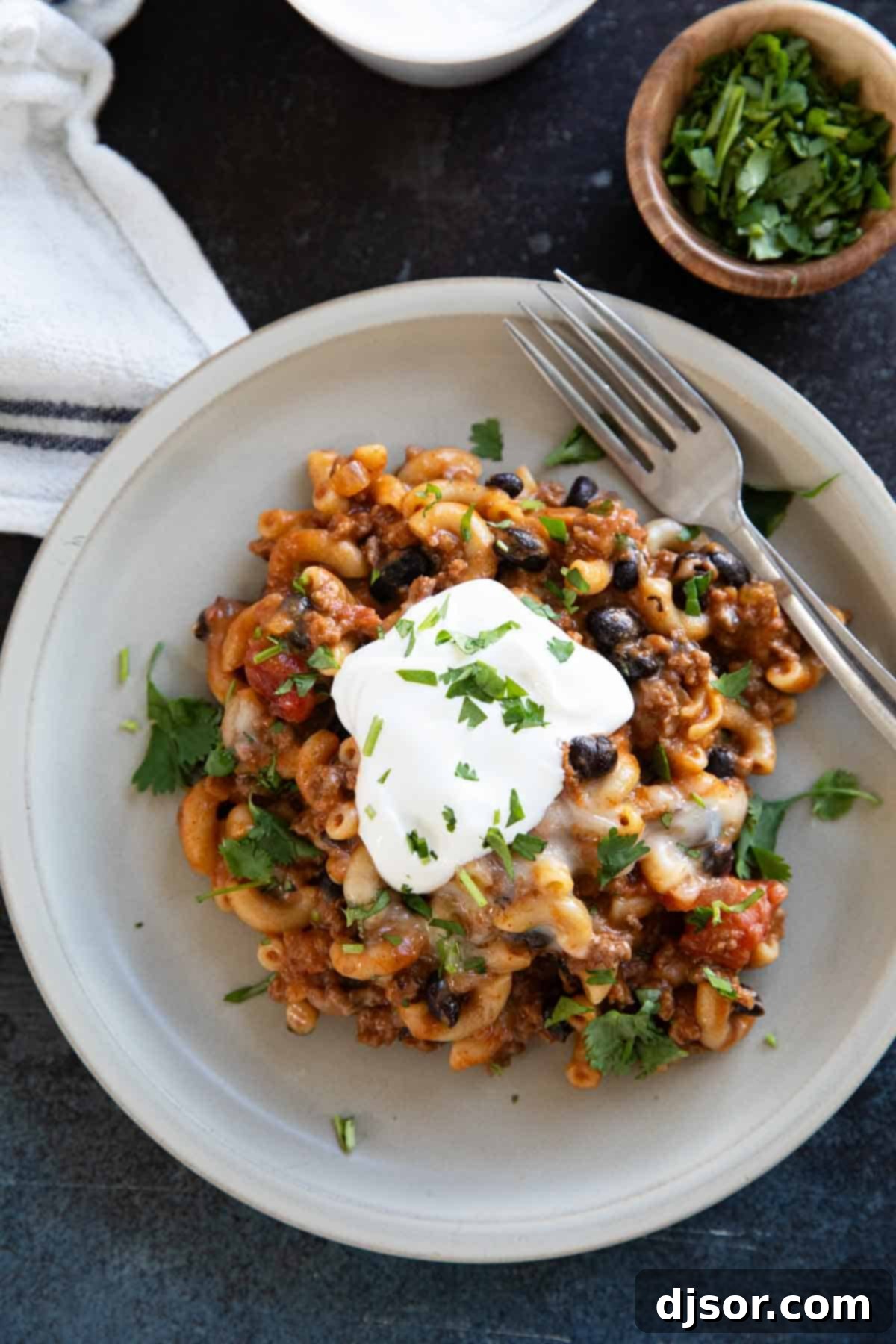 Classic Chili Mac with black beans, topped with a dollop of sour cream and fresh chopped cilantro, served in a rustic bowl.