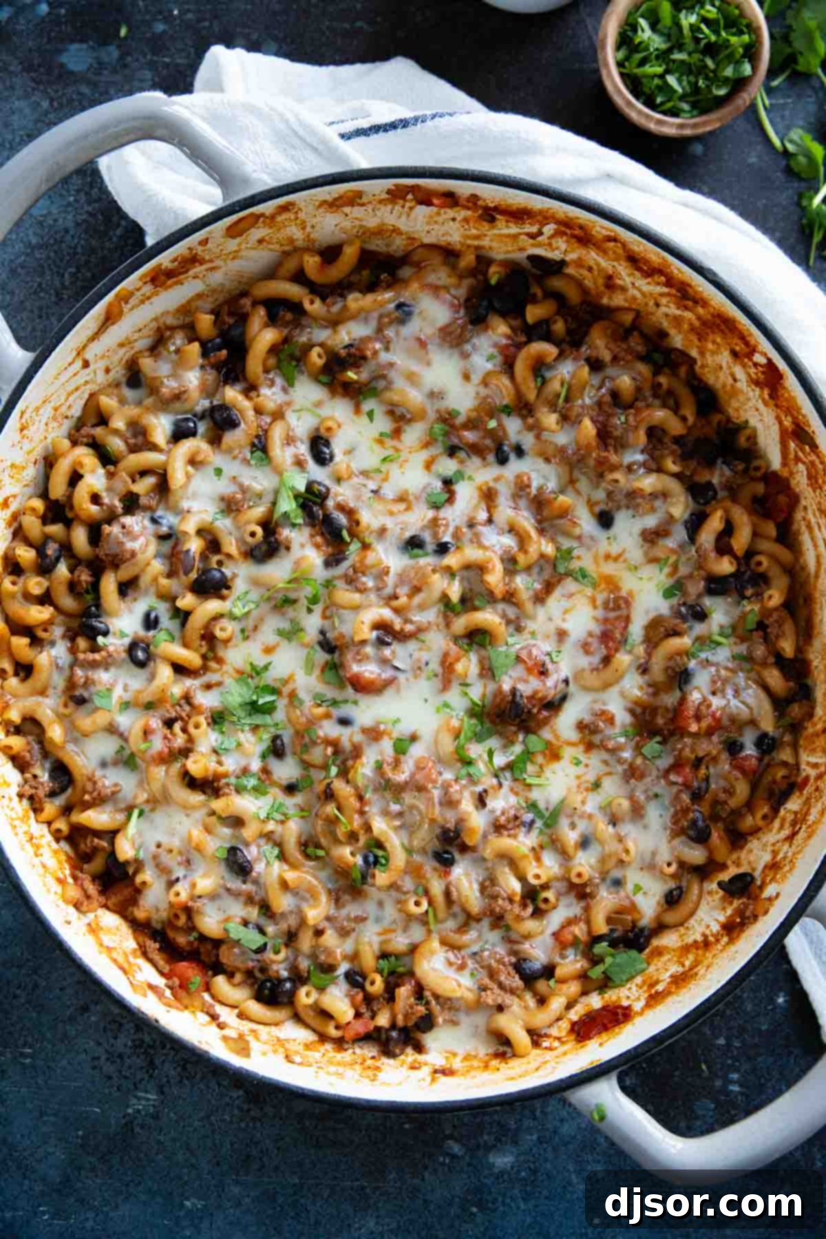 A finished casserole dish of homemade One-Pan Chili Mac, topped with a generous layer of melted cheese and garnished with fresh cilantro, ready to be served.