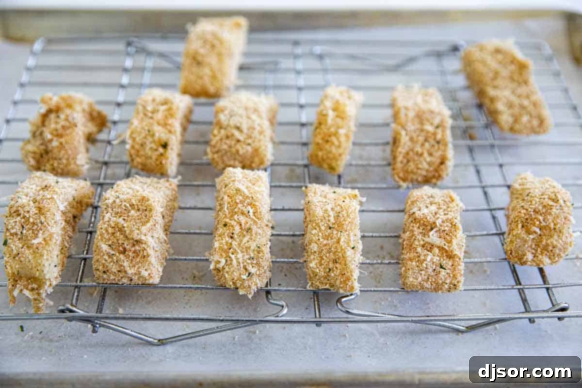 Coated fish sticks neatly arranged on a cooling rack placed over a baking sheet, ready for the oven.