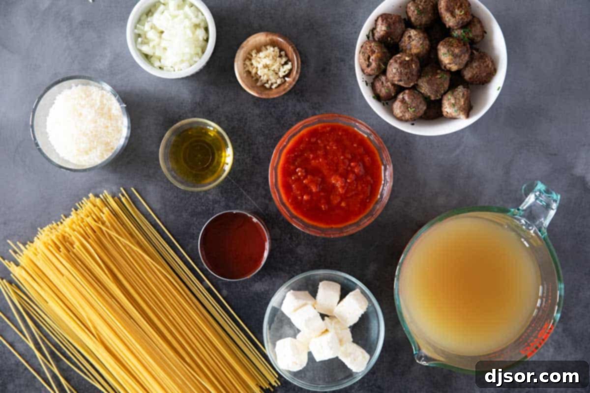 One Pan Creamy Meatball Spaghetti 3 A selection of fresh ingredients laid out on a white surface, including olive oil, onions, garlic, broth, marinara, tomato sauce, spaghetti, cream cheese, parmesan, and meatballs for Creamy One Pot Spaghetti with Meatballs.