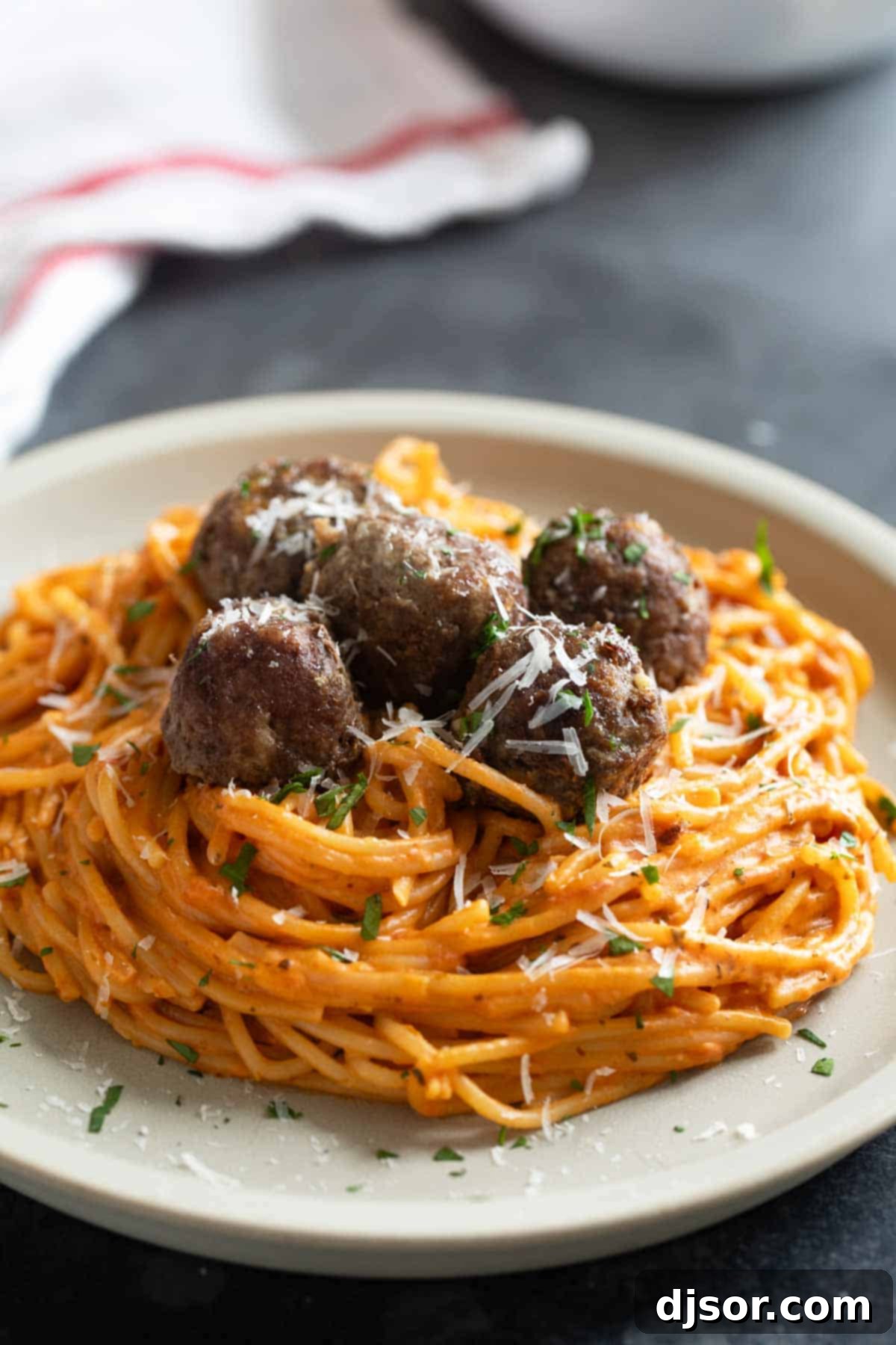 One Pan Creamy Meatball Spaghetti 7 A white plate generously filled with Creamy One Pot Spaghetti, topped with savory meatballs and a sprinkle of fresh parsley.