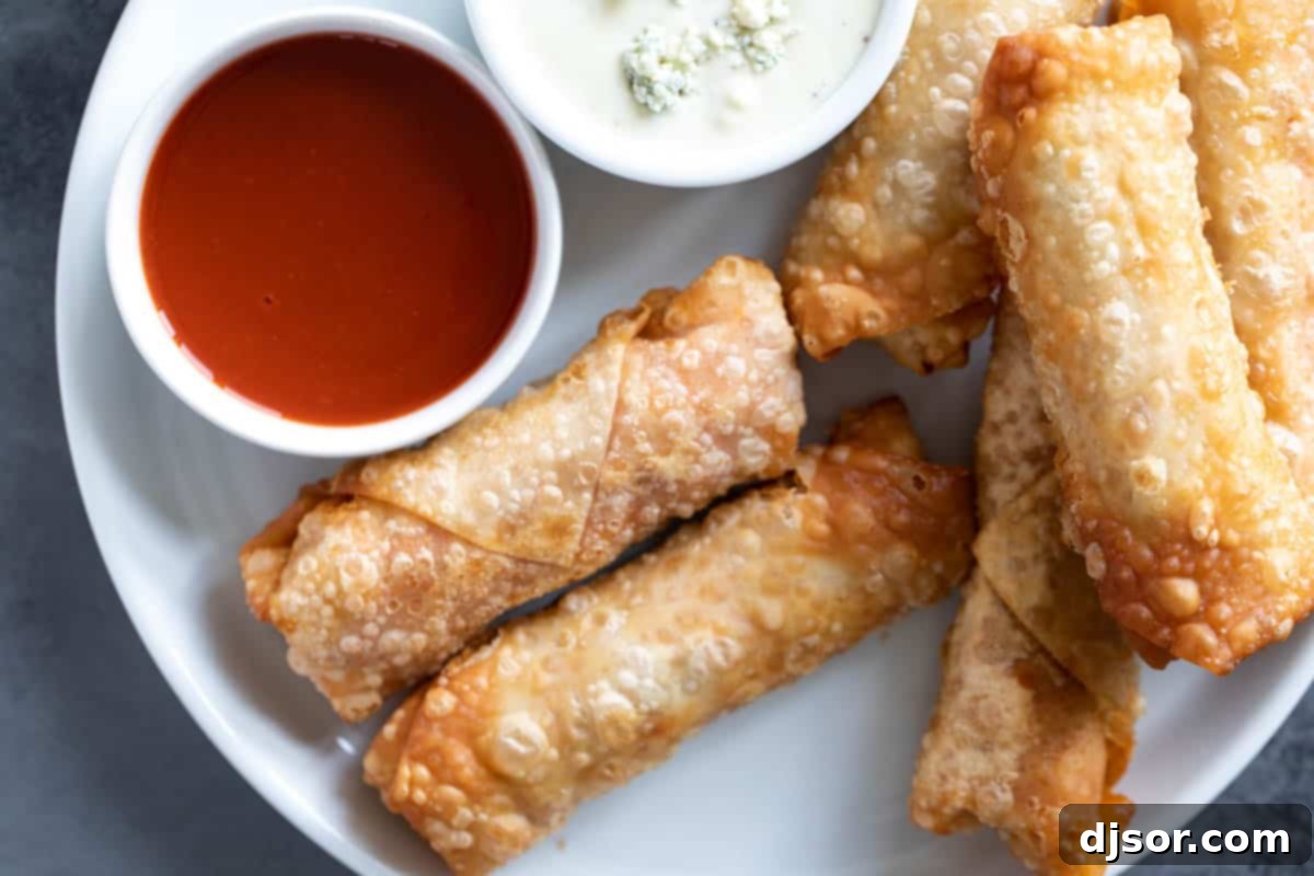 Perfect for a game day appetizer or meal, these Buffalo Chicken Egg Rolls have crisp outer shells that are filled with chicken, hot sauce, blue cheese, and slaw. Plate with buffalo chicken egg rolls with dipping sauces.