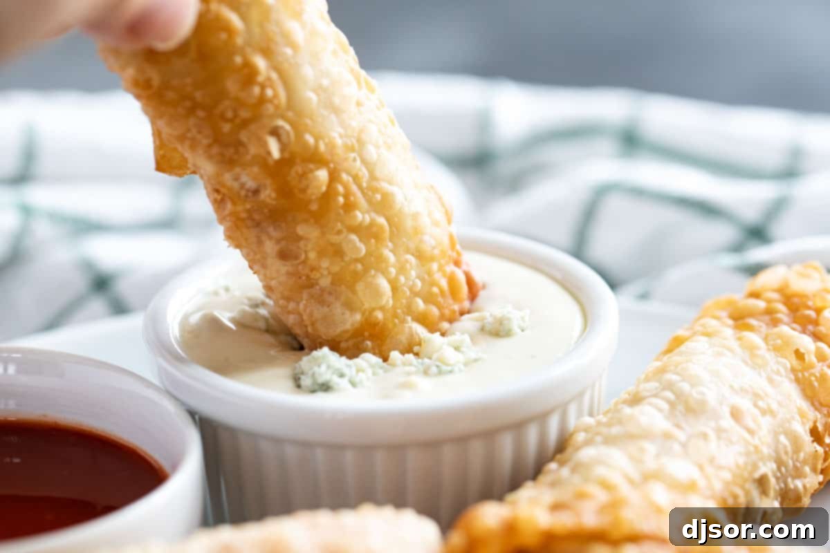 Perfect for a game day appetizer or meal, these Buffalo Chicken Egg Rolls have crisp outer shells that are filled with chicken, hot sauce, blue cheese, and slaw. Dipping a buffalo chicken egg roll into blue cheese dressing.