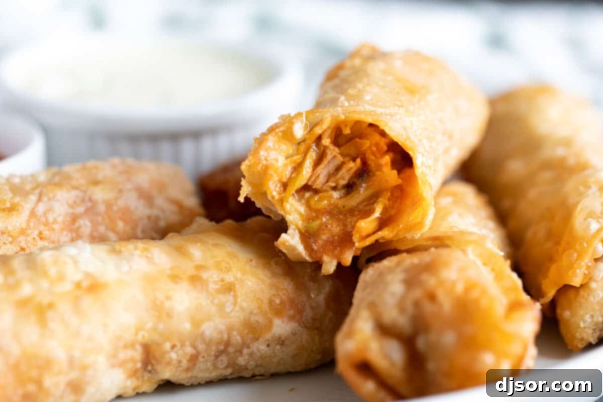 Perfect for a game day appetizer or meal, these Buffalo Chicken Egg Rolls have crisp outer shells that are filled with chicken, hot sauce, blue cheese, and slaw. Buffalo Chicken Egg Rolls with a bite taken from one roll.