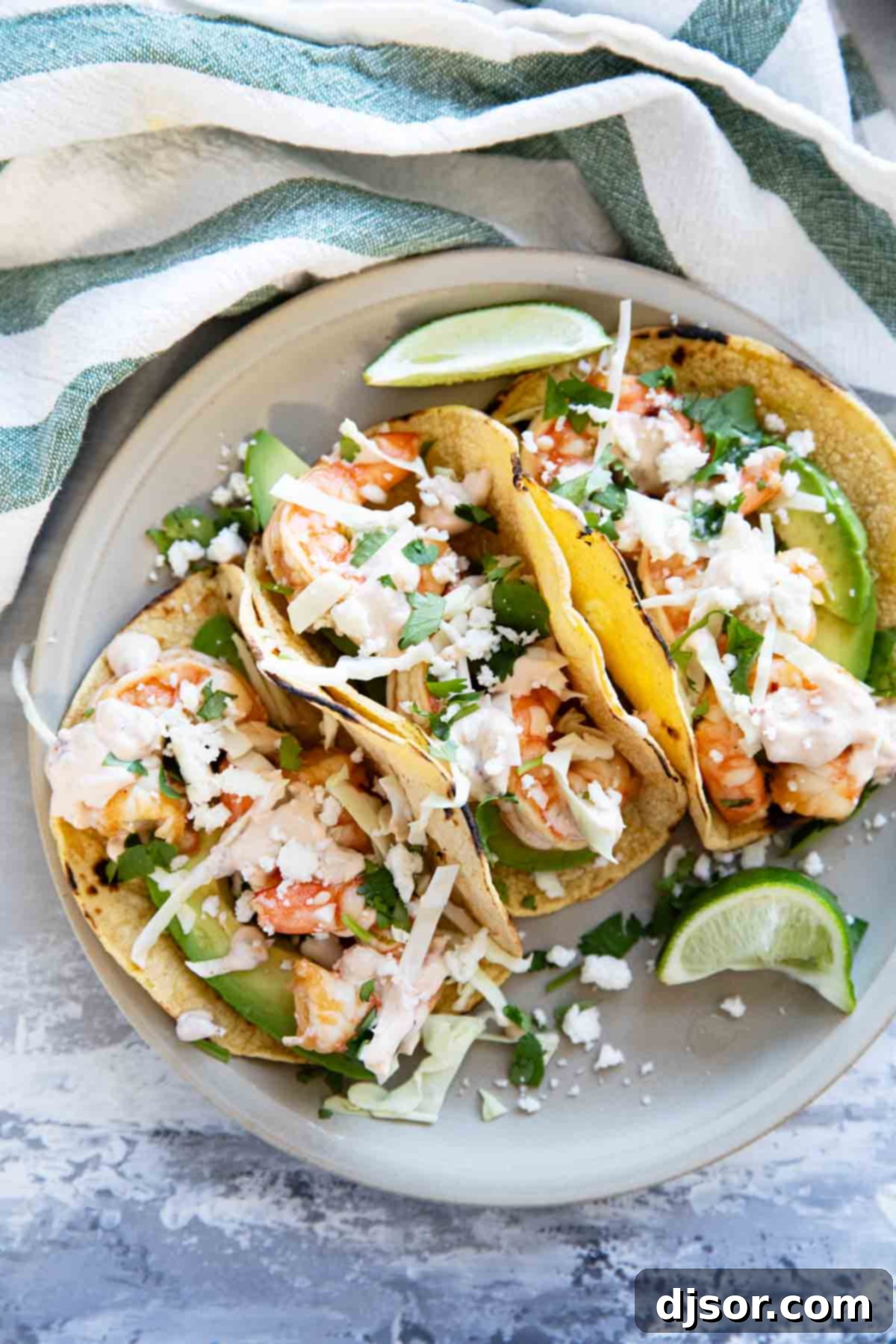 Three shrimp tacos on a plate, topped with cabbage, cheese, and chipotle lime crema.