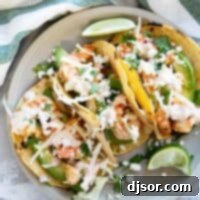 Three shrimp tacos on a plate, topped with cabbage, cheese, and chipotle lime crema.