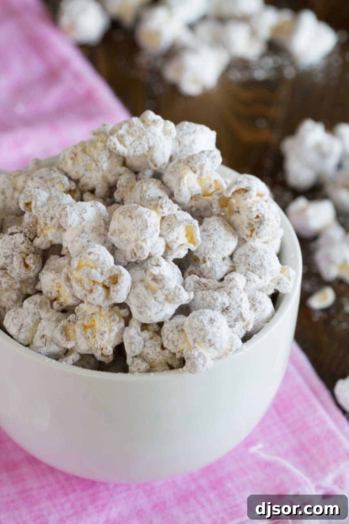 A beautifully arranged white bowl overflowing with delicious Muddy Buddy Popcorn, ready to be enjoyed.