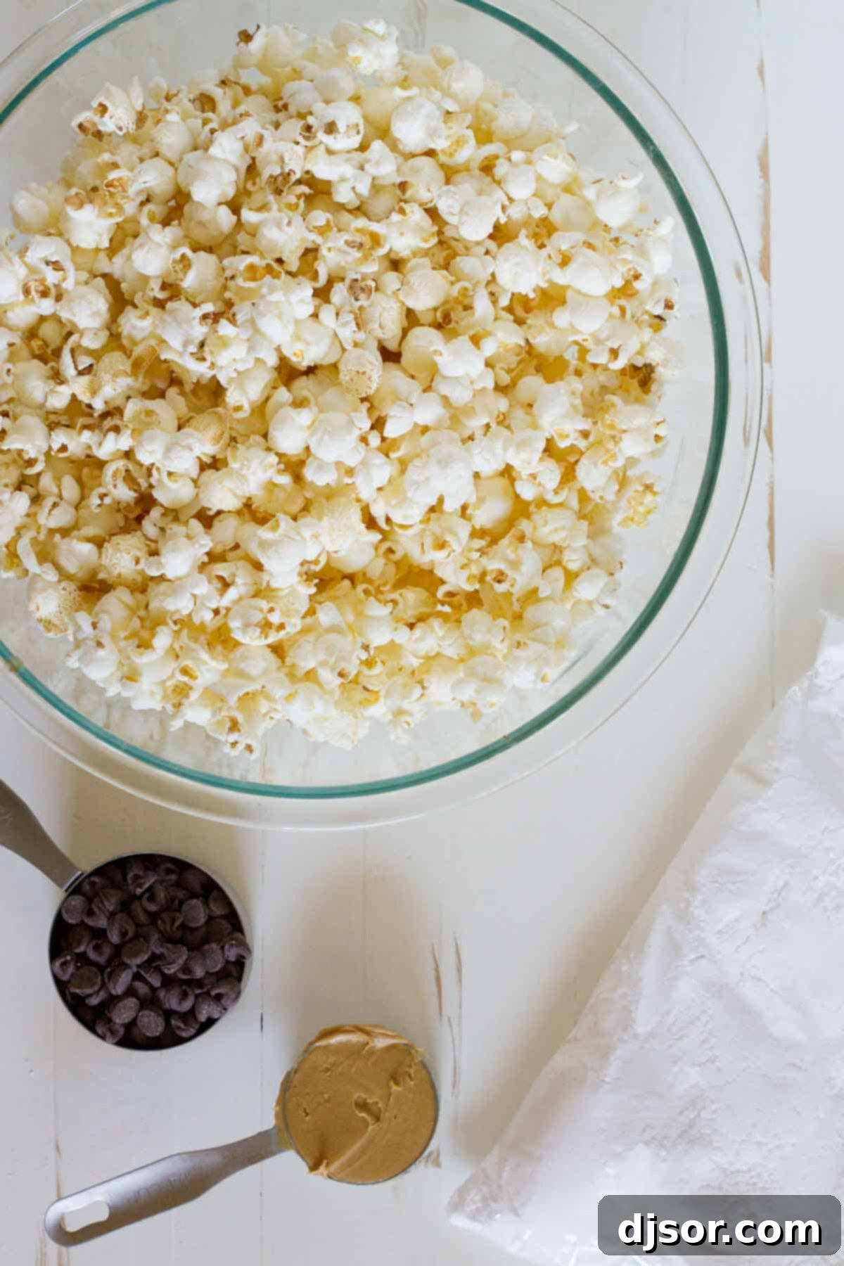 All the essential ingredients for making Muddy Buddy Popcorn laid out neatly on a counter.
