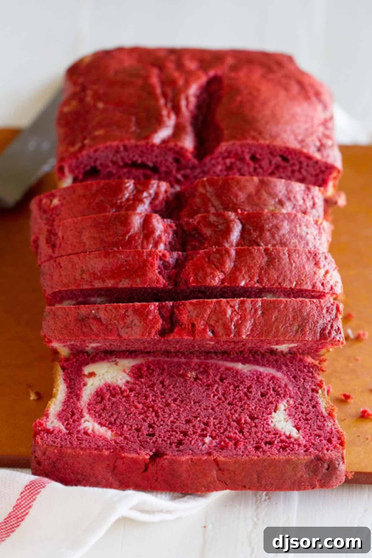 Sliced loaf of Red Velvet Quick Bread with Cream Cheese Filling - showing the cut side of one slice, revealing the vibrant red bread and creamy white filling.