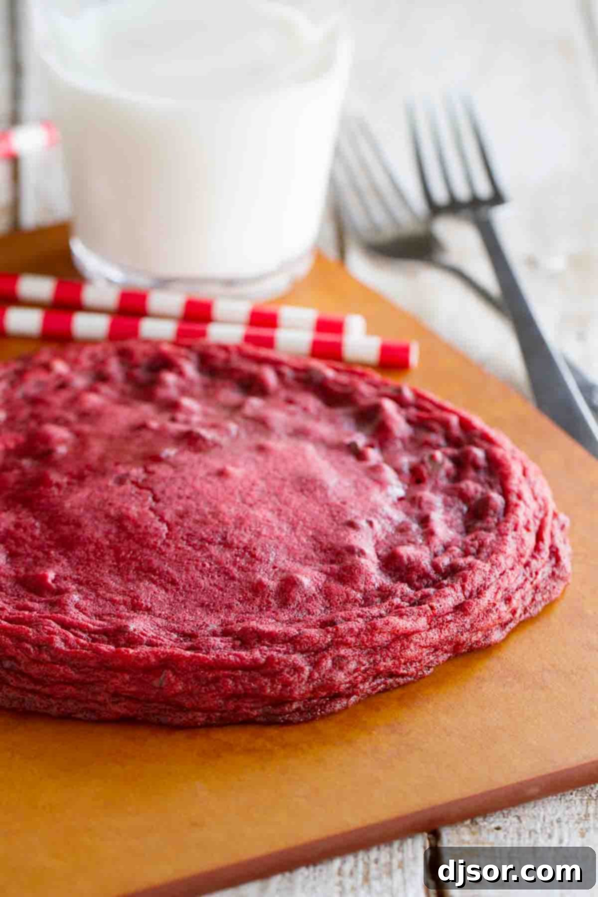 XL Red Velvet Cookie on a cutting board with milk behind, showcasing its impressive size and rich color.