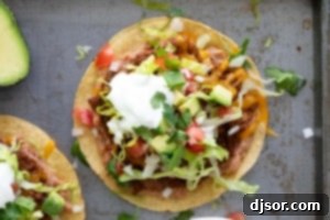 Beef Tostadas topped with lettuce, tomatoes, sour cream, and cilantro.