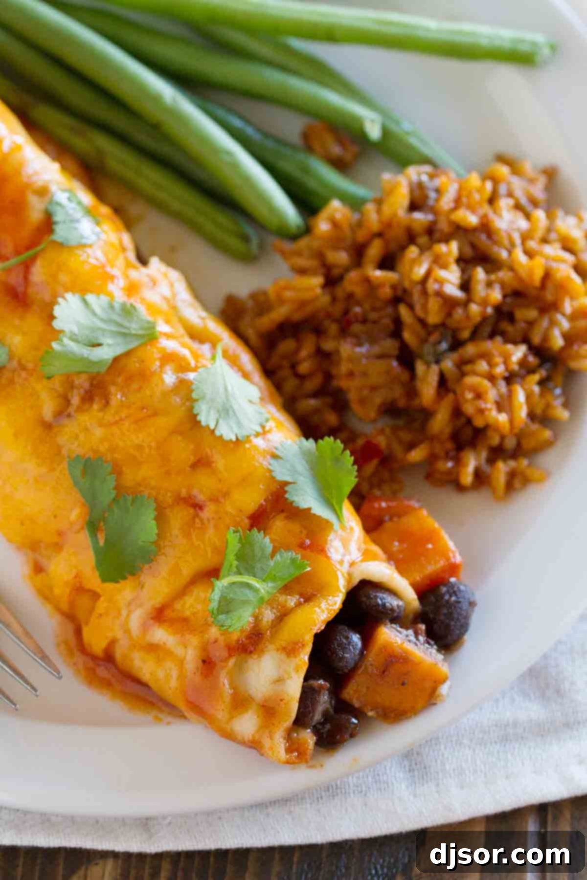 A close-up shot of a single vegetarian enchilada, revealing the rich filling of sweet potatoes and black beans, perfectly wrapped in a tortilla and covered in sauce and cheese.