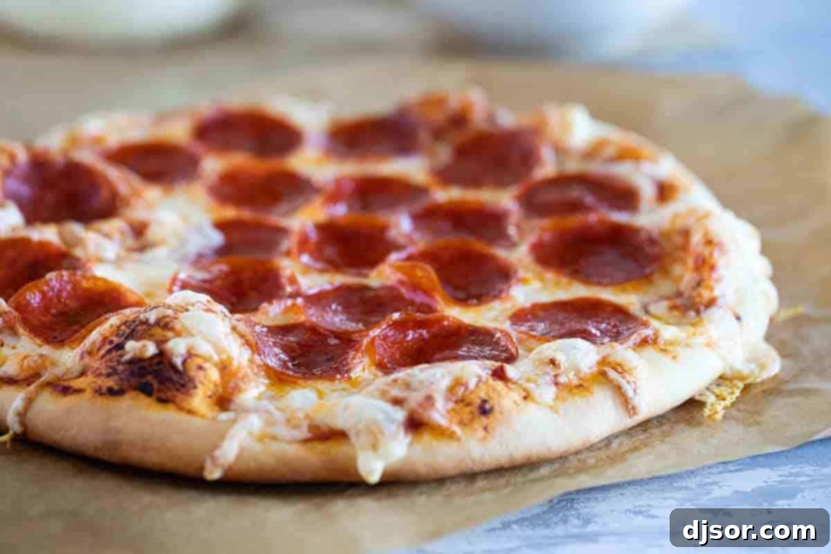 A freshly baked pepperoni pizza on parchment paper, with a perfectly browned crust and melted cheese, ready to be sliced and served.