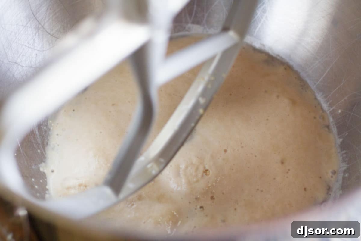 Warm water, sugar, and yeast combined in a mixing bowl, beginning to froth and activate.