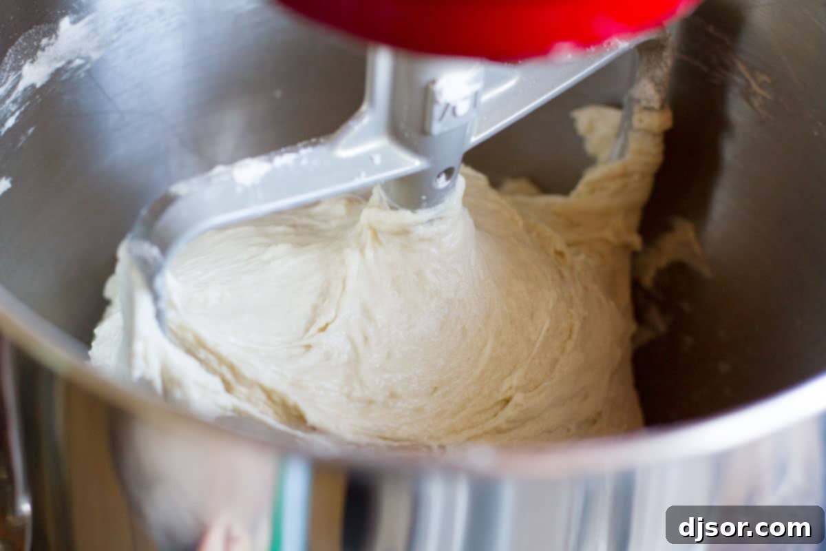 The mixing pizza dough still looks wet and sticky in the stand mixer bowl, indicating proper consistency for the recipe's unique method.