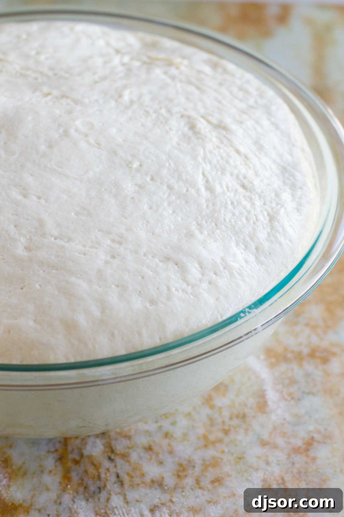 A bowl of pizza dough, covered with a towel, rising in a warm environment until doubled in size.