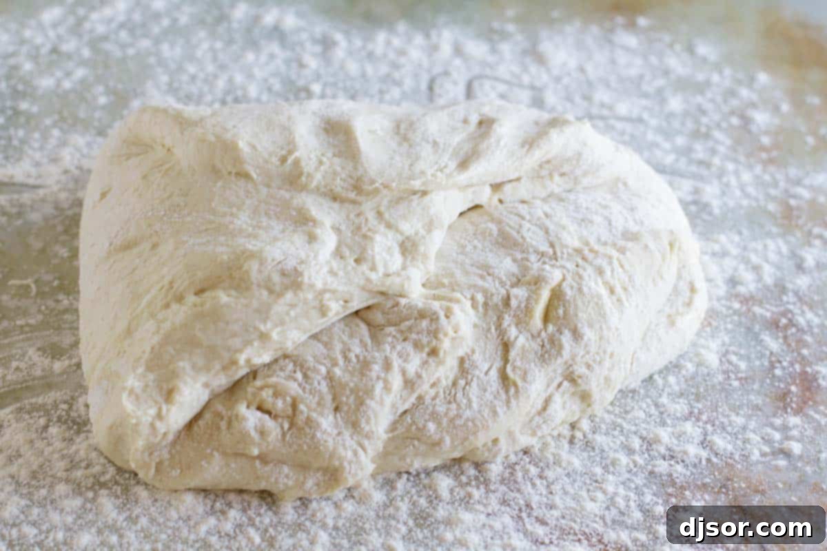 Hands gently pulling and gathering the pizza dough, shaping it into a smooth ball on a floured surface.