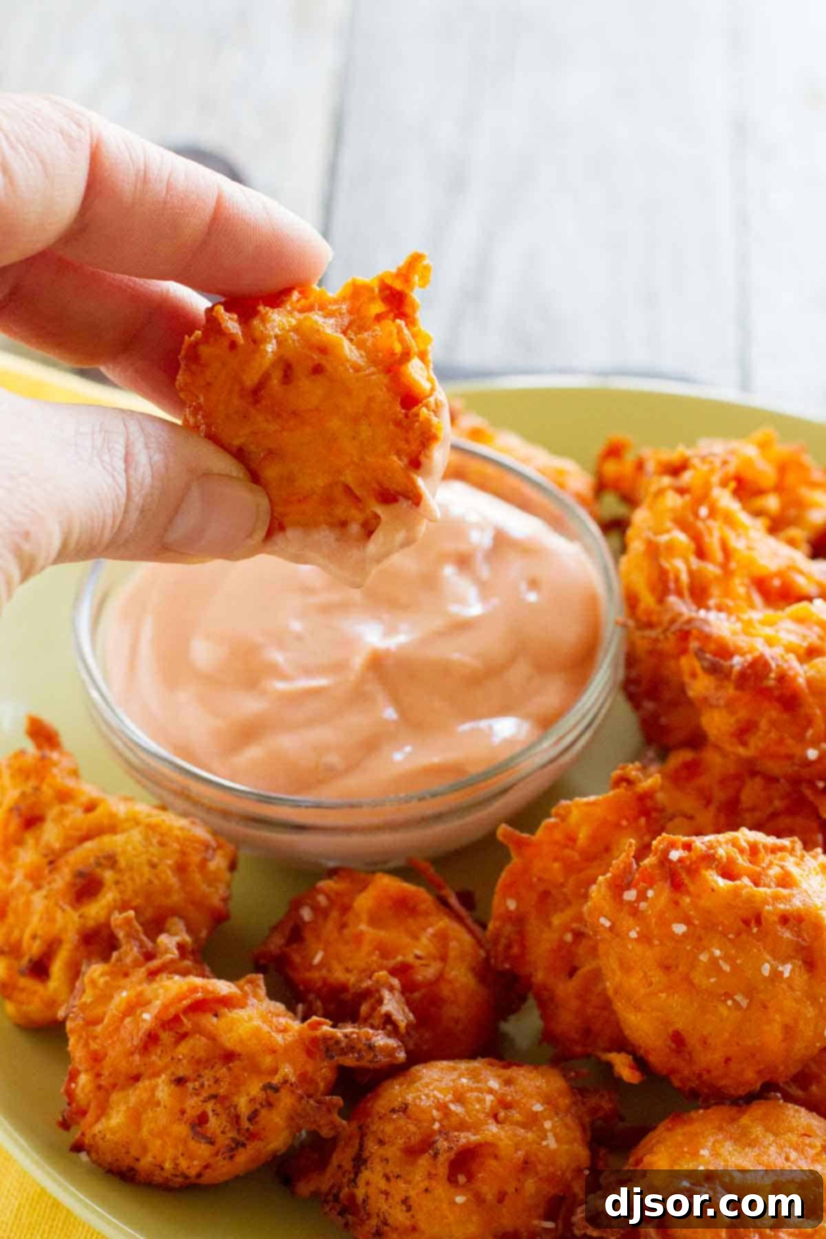 Golden Sweet Potato Tots with Velvety Ketchup 4 A hand dipping a single, golden Sweet Potato Tot into a dollop of creamy ketchup, clearly showcasing the crispy exterior and inviting texture.