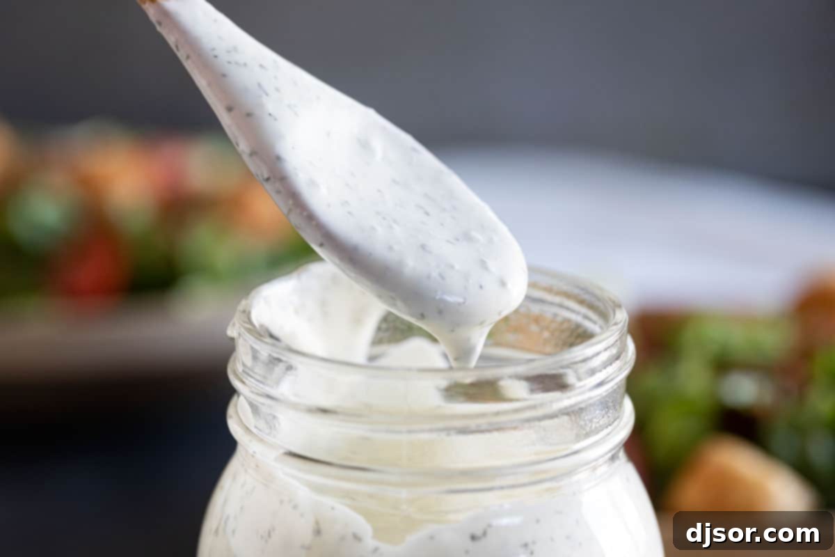 A spoonful of rich, creamy homemade ranch dressing being drizzled over a mason jar, highlighting its perfect texture.