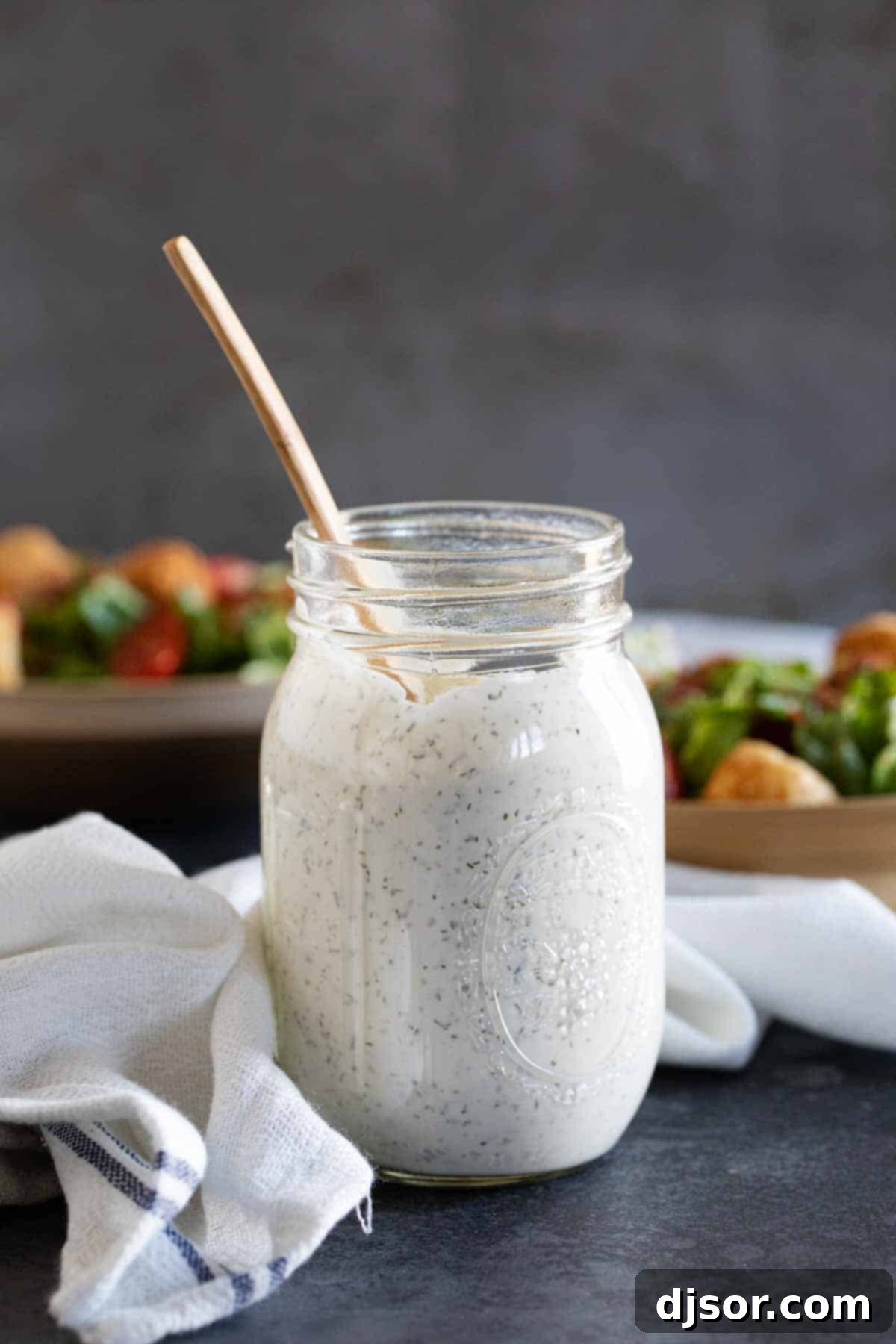 A mason jar filled with creamy homemade ranch dressing, placed on a table with fresh salads in the background, ready for a healthy meal.