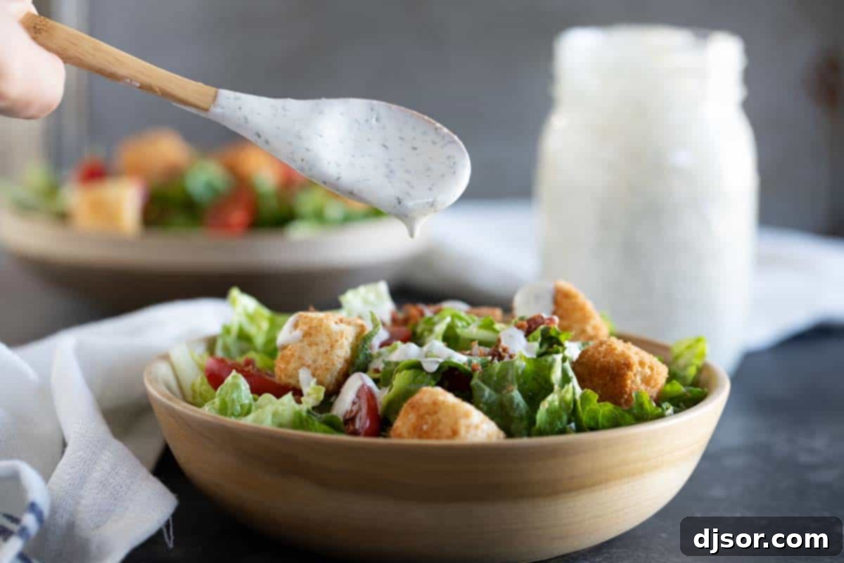 A hand spooning creamy homemade ranch dressing generously over a vibrant green salad in a white bowl, showing its perfect consistency.