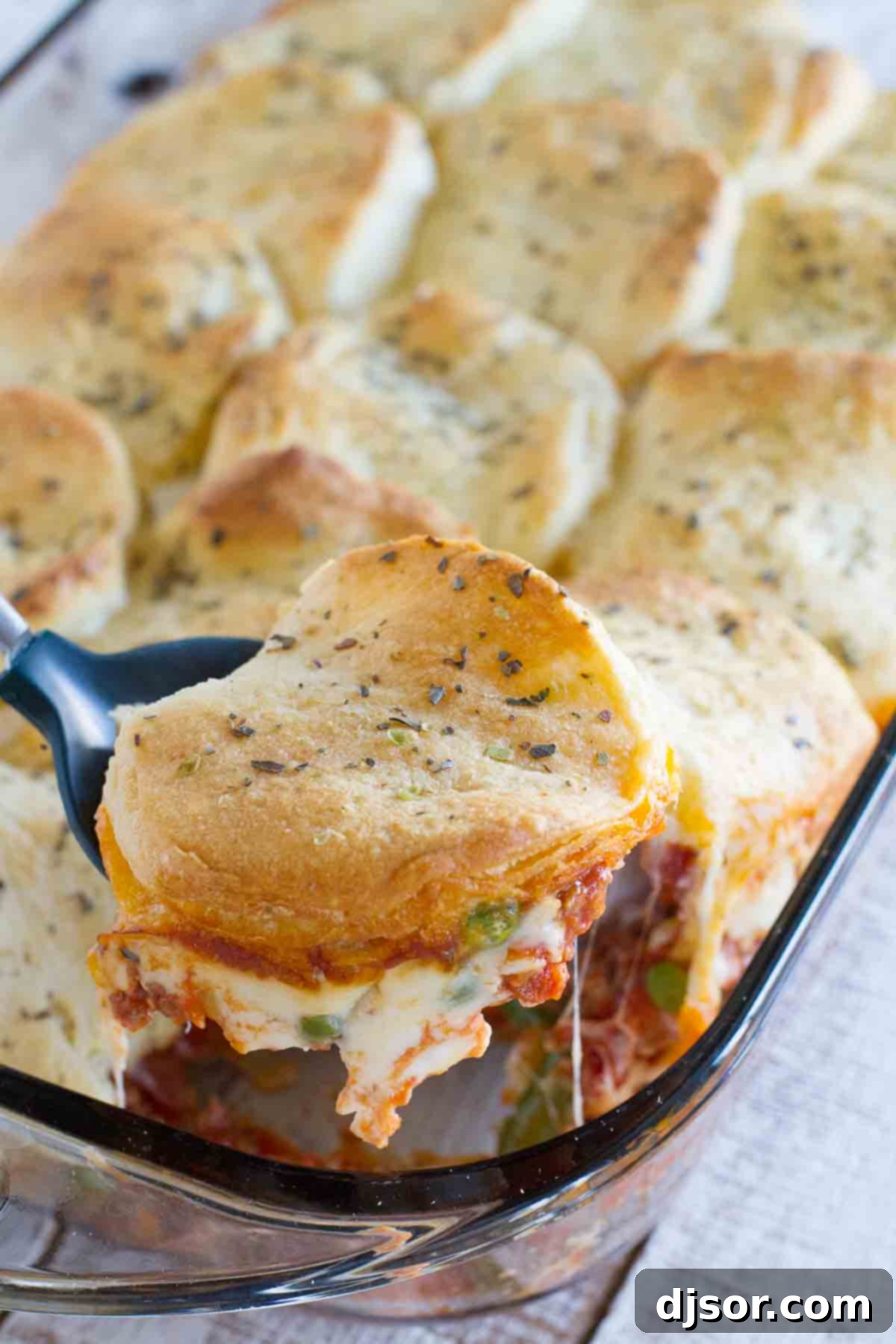 A generous serving of Italian Ground Beef Casserole with golden biscuit topping being removed from a baking dish, showcasing its rich layers and inviting texture.