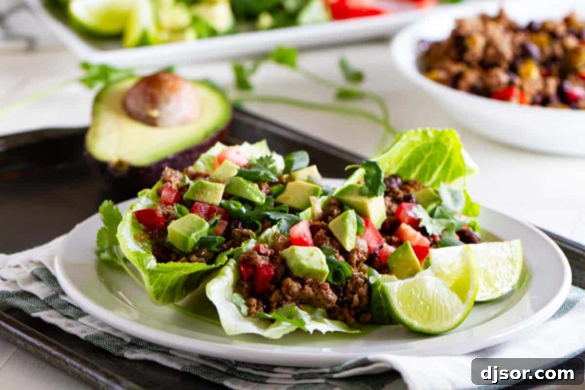 Taco lettuce wraps on a white plate with more filling behind them.